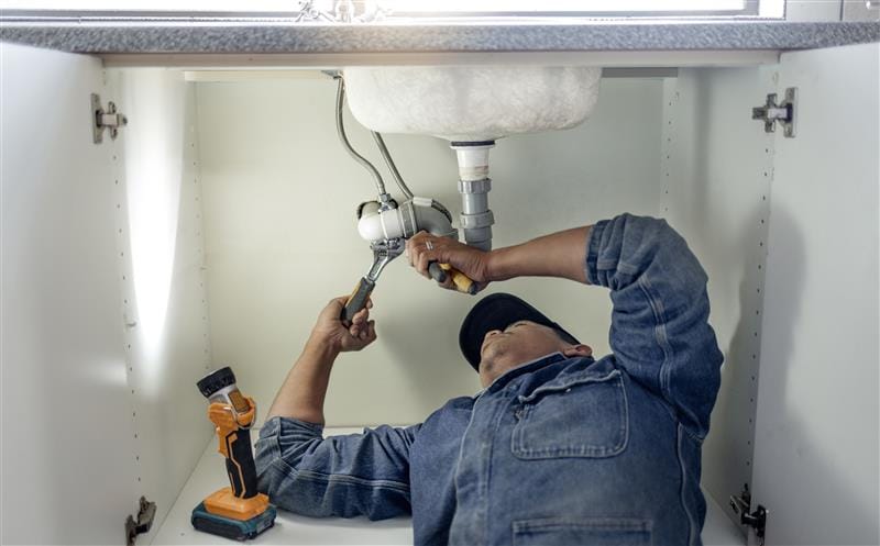 Plumber repairing pipes beneath a bathroom sink in Pensacola
