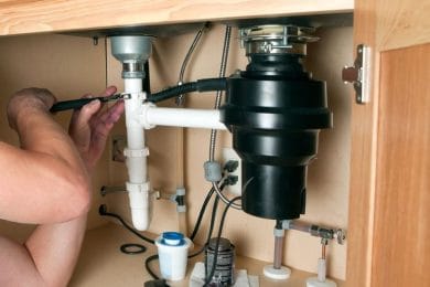 Plumber repairing a garbage disposal beneath a kitchen sink in Pensacola