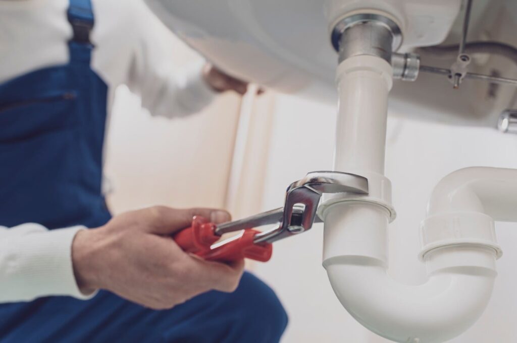Plumber repairing a white drain pipe beneath a sink in Pensacola