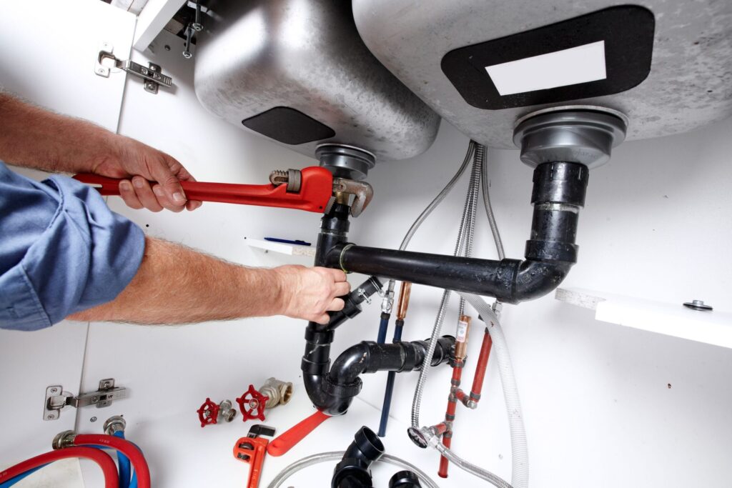 Plumber repairing drain pipes beneath a kitchen sink in Pensacola